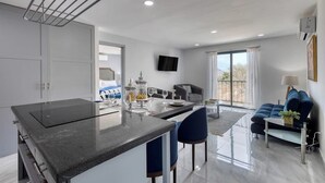 A modern kitchen with a central island, a dining area with a sofa and table, and a living room with a couch and a TV. - Hotel Suite With Ocean-view Rooftop Infinity Pool, Balconies & AC (Cabo San Lucas)