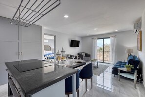 A modern kitchen with a central island, a dining area with a sofa and table, and a living room with a couch and a TV. - Hotel Suite With Ocean-view Rooftop Infinity Pool, Balconies & AC (Cabo San Lucas)