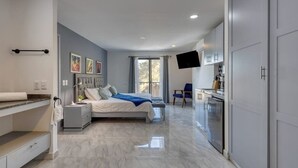 A modern bedroom with a bed, bedside tables, a flat-screen TV, and a bathroom with a shower and toilet. - Hotel Suite With Ocean-view Rooftop Infinity Pool, Balconies & AC (Cabo San Lucas)