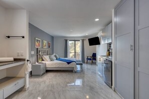 A modern bedroom with a bed, bedside tables, a flat-screen TV, and a bathroom with a shower and toilet. - Hotel Suite With Ocean-view Rooftop Infinity Pool, Balconies & AC (Cabo San Lucas)