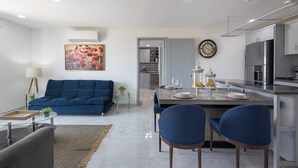 A modern living room with a blue sofa, a dining area with a table set for two, and a kitchen with stainless steel appliances. - Hotel Suite With Ocean-view Rooftop Infinity Pool, Balconies & AC (Cabo San Lucas)