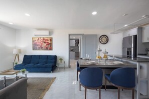 A modern living room with a blue sofa, a dining area with a table set for two, and a kitchen with stainless steel appliances. - Hotel Suite With Ocean-view Rooftop Infinity Pool, Balconies & AC (Cabo San Lucas)