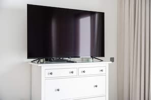 A flat-screen TV mounted on a white cabinet with drawers, positioned against a wall with a curtain. - Free Housekeeping Visits During Your Stay - Stayshort - Modern 4 BR Villa in Damac Hills 2 With Garden That Sleeps 8 (Dubai)