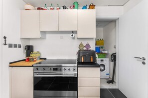 A compact kitchen with a stove, oven, washing machine, and a small countertop. - Free Housekeeping Visits During Your Stay - Stayshort - Modern 4 BR Villa in Damac Hills 2 With Garden That Sleeps 8 (Dubai)