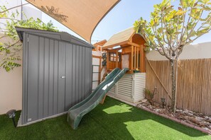 A backyard with a slide, a fenced area, and a tree. - Free Housekeeping Visits During Your Stay - Stayshort - Modern 4 BR Villa in Damac Hills 2 With Garden That Sleeps 8 (Dubai)