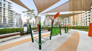 An outdoor playground with climbing structures and a seating area, surrounded by modern buildings and greenery. - Free Housekeeping Visits During Your Stay - Stayshort - Bright 2 Bedroom in Madinat Jumeirah Living That Sleeps 6 With Balcony (Dubai)