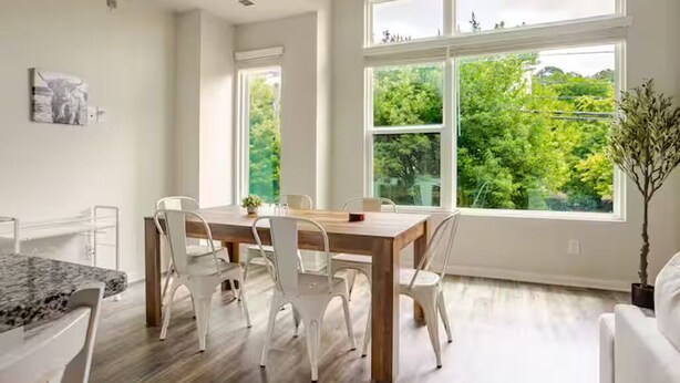 Un'area pranzo moderna con un tavolo di legno e sedie bianche, ampie finestre che si affacciano sul verde e un'arredamento minimalista.