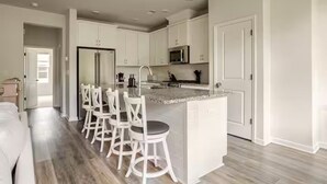 Una cucina moderna con mobili bianchi, un piano di lavoro in granito e un'isola integrata con sgabelli da bar.