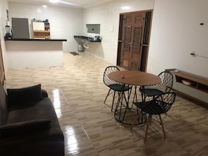 A compact living space with a dining area, a sofa, a kitchen with a built-in fridge, and a wooden door.