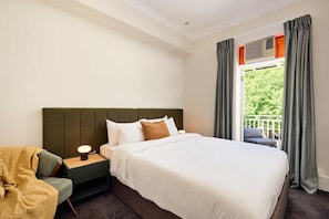 Habitació d'hotel amb llit, una tauleta de nit, una làmpada, una cadira i una finestra amb cortines.