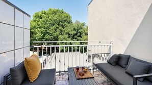 Un balcon avec un canapé, une table sur laquelle se trouve un plateau de nourriture et une vue sur les arbres.