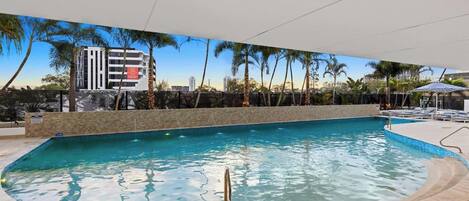 Une piscine offrant une vue dégagée sur les environs, notamment sur un immeuble à plusieurs étages et des palmiers.