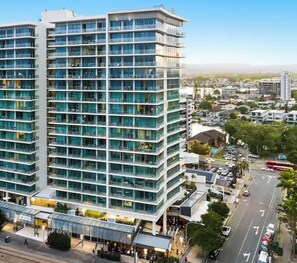 Et moderne hotel med flere etager og en glasfacade, beliggende i et byområde med en travl gade og andre bygninger i baggrunden.