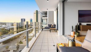 En balkon med udsigt over byen, en sofa, et spisebord med frugt og et fjernsyn.