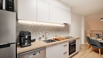 A modern kitchen with a built-in coffee machine, a sink, a dishwasher, and a dining area with chairs.