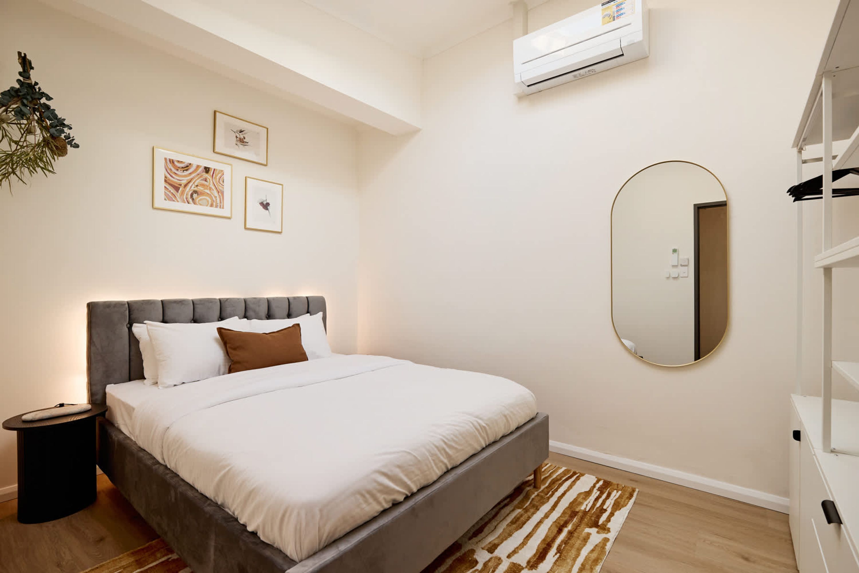 A bedroom with a bed, a bedside table, a mirror, and wall-mounted artwork.