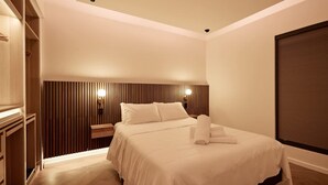 Una habitació d'hotel amb llit, taules de nit, un panell de fusta al capçal del llit i una finestra amb persianes.