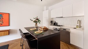 Cuina moderna amb armaris blancs, una illa de taulell negre i una zona de dinar amb tamborets.