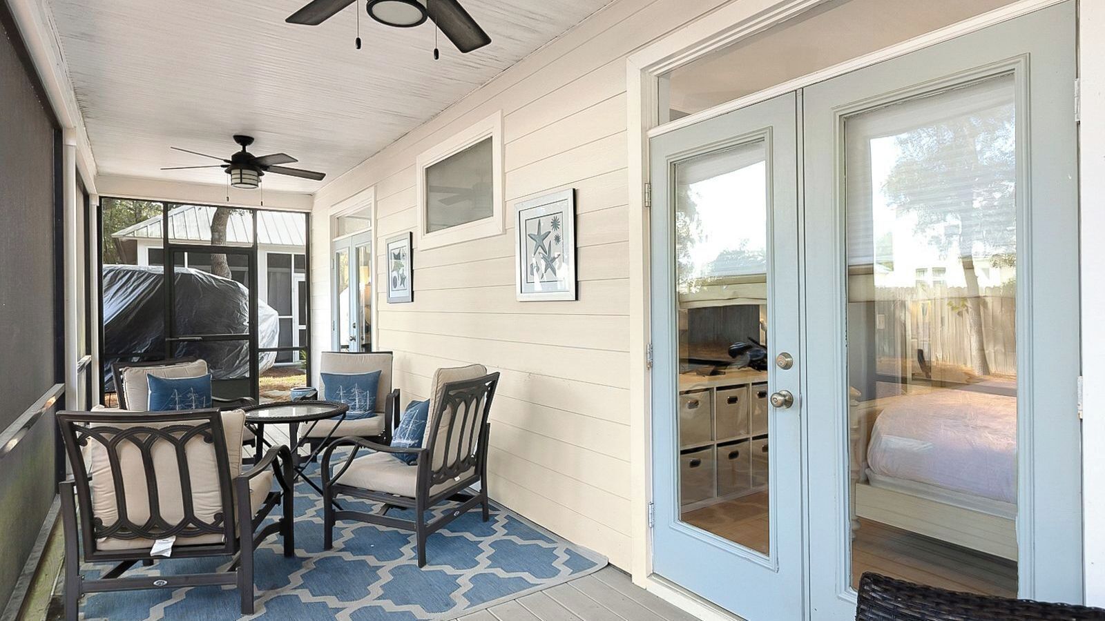 A covered porch with a ceiling fan, a table with chairs, and a sliding glass door leading to a bedroom.