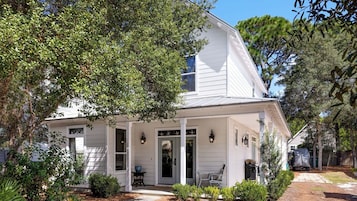 A white two-story house with a porch, a small front yard, and a covered vehicle in the background.