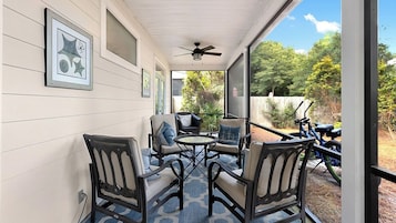 A covered patio with outdoor furniture, a ceiling fan, and a view of a bicycle in the background.
