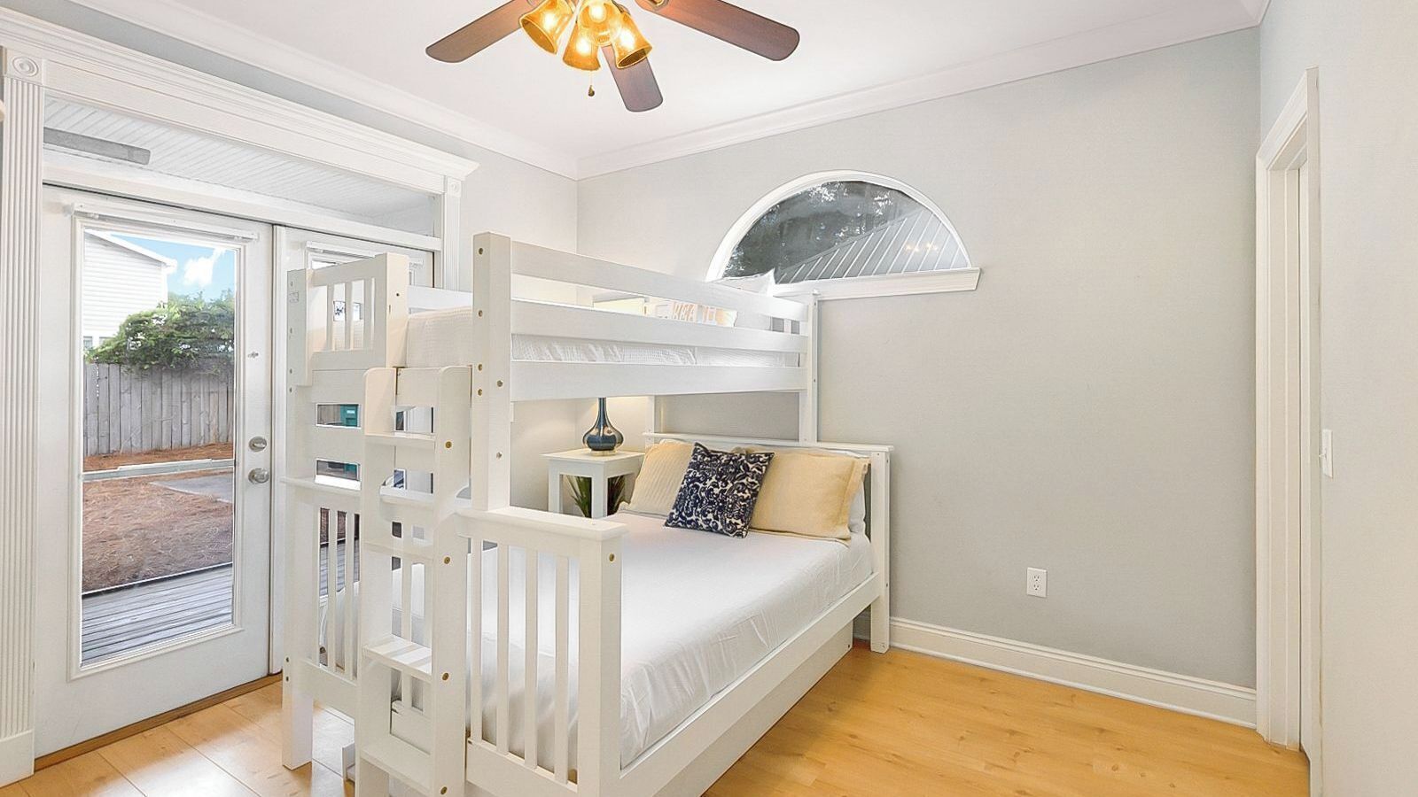 A bedroom with a bunk bed, a small table, a lamp, and a fan.