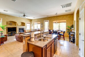 A spacious living area with a fireplace, a large island with a sink, and a dining area with chairs and a table. - Private Pool & Hot Tub | Pet-Friendly Escape! (Maricopa)