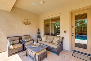 A sunlit patio area with wicker furniture, a cushioned sofa, and a decorative wall piece. - Private Pool & Hot Tub | Pet-Friendly Escape! (Maricopa)