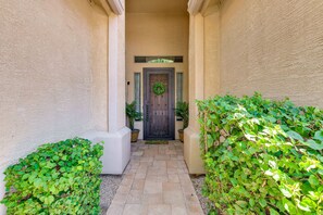 A narrow pathway leading to a door with a wreath, flanked by potted plants and a textured wall. - Private Pool & Hot Tub | Pet-Friendly Escape! (Maricopa)