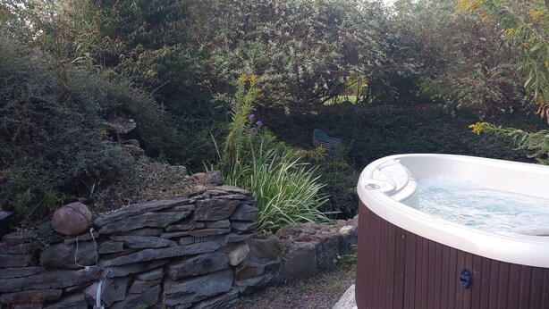 A hot tub surrounded by a stone wall and lush greenery. - Romantic couples bed & breakfast in secluded Strykersville NY (STRYKERSVILLE)