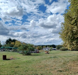 A rural landscape with a grassy field, a wooden structure, and a house in the distance.