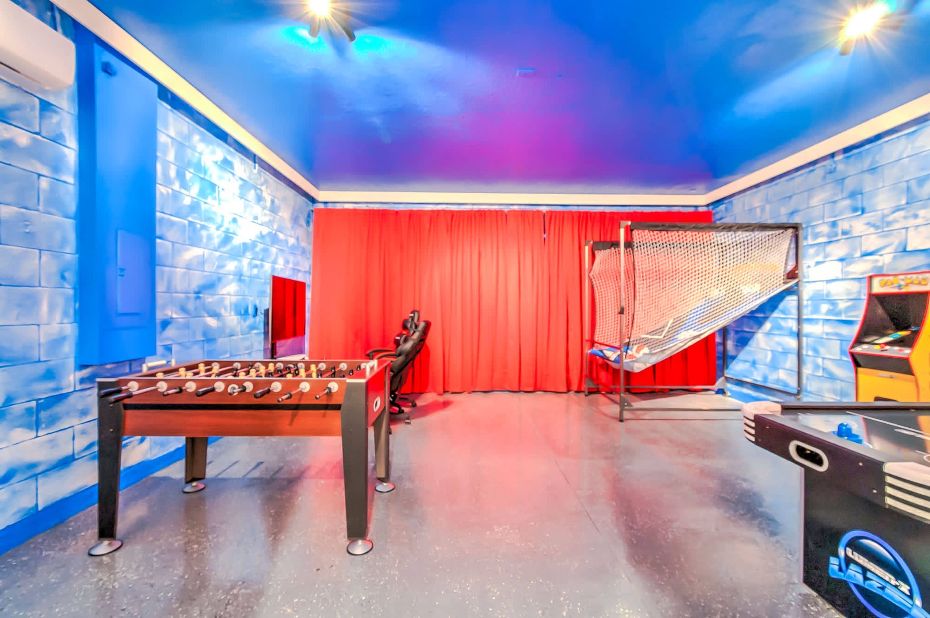 Una habitación con mesa de fútbol de mesa, cortina roja y una zona delimitada con red, probablemente para actividades deportivas.
