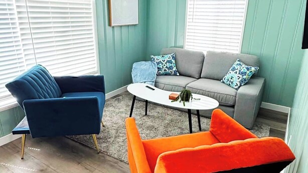 A room with teal walls, a grey sofa, a blue armchair, and an orange armchair. - Charming Beach Cottage (San Diego)