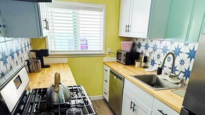 A compact kitchen with a gas stove, a microwave, a sink, and a dishwasher. - Charming Beach Cottage (San Diego)