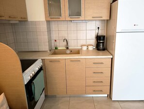 A kitchen with wooden cabinets, a sink, a stove, and a coffee maker. - Καλωσορίσατε στο Helen’s Cozy Escape, ένα πολυτελές και κομψό studio. (Nea Michaniona)