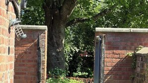 A gated entrance with a brick wall, a metal gate, and a potted plant. - Park4Free - Etihad & Co-op Live near- Nifty Find (Manchester)