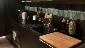 Una cucina moderna con mobili scuri, un piano di lavoro nero, un tagliere di legno e una parete di fondo rivestita di piastrelle.