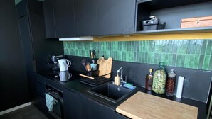 Una cucina moderna con mobili scuri, uno schienale piastrellato verde e un piano di lavoro in legno, e diversi elettrodomestici.