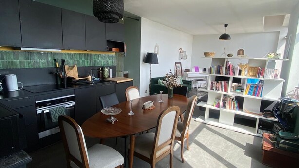 Una cucina moderna con mobili scuri, un tavolo da pranzo con sedie e una libreria piena di libri.
