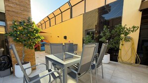 An outdoor patio with a glass table and chairs, surrounded by potted plants and a yellow wall. - ALYOUISIFYIACHALET (amman)