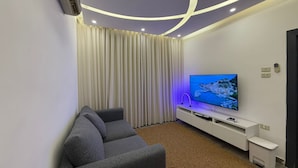 A modern living room with a flat-screen TV, grey sofa, and white entertainment unit. - ALYOUISIFYIACHALET (amman)