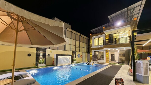 A swimming pool with lounge chairs, a covered area, and a two-story building with a balcony. - ALYOUISIFYIACHALET (amman)