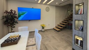 A modern living room with a flat-screen TV, a chessboard, a staircase, and a bookshelf. - ALYOUISIFYIACHALET (amman)