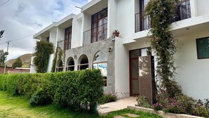 A two-story building with a white facade, arched windows, and a balcony with a potted plant. - Casa Ymelda Desaguadero (Desaguadero)