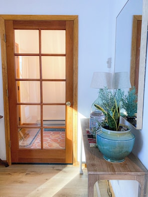 Eine Holztür mit Fensterglas, ein Blumentopf, eine Lampe und ein kleiner Tisch mit Spiegel.