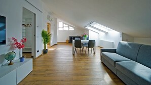 En moderne stue med en sofa, et spisebord med stole, et fjernsyn og en potteplante.