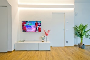 Ein modernes Wohnzimmer mit einem Wand-Fernseher, einem weißen Konsolentisch, einem Globus und einer Zimmerpflanze.