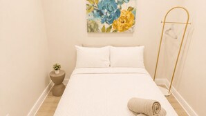 Quarto com cama, quadro, mesa de cabeceira, planta e toalha.