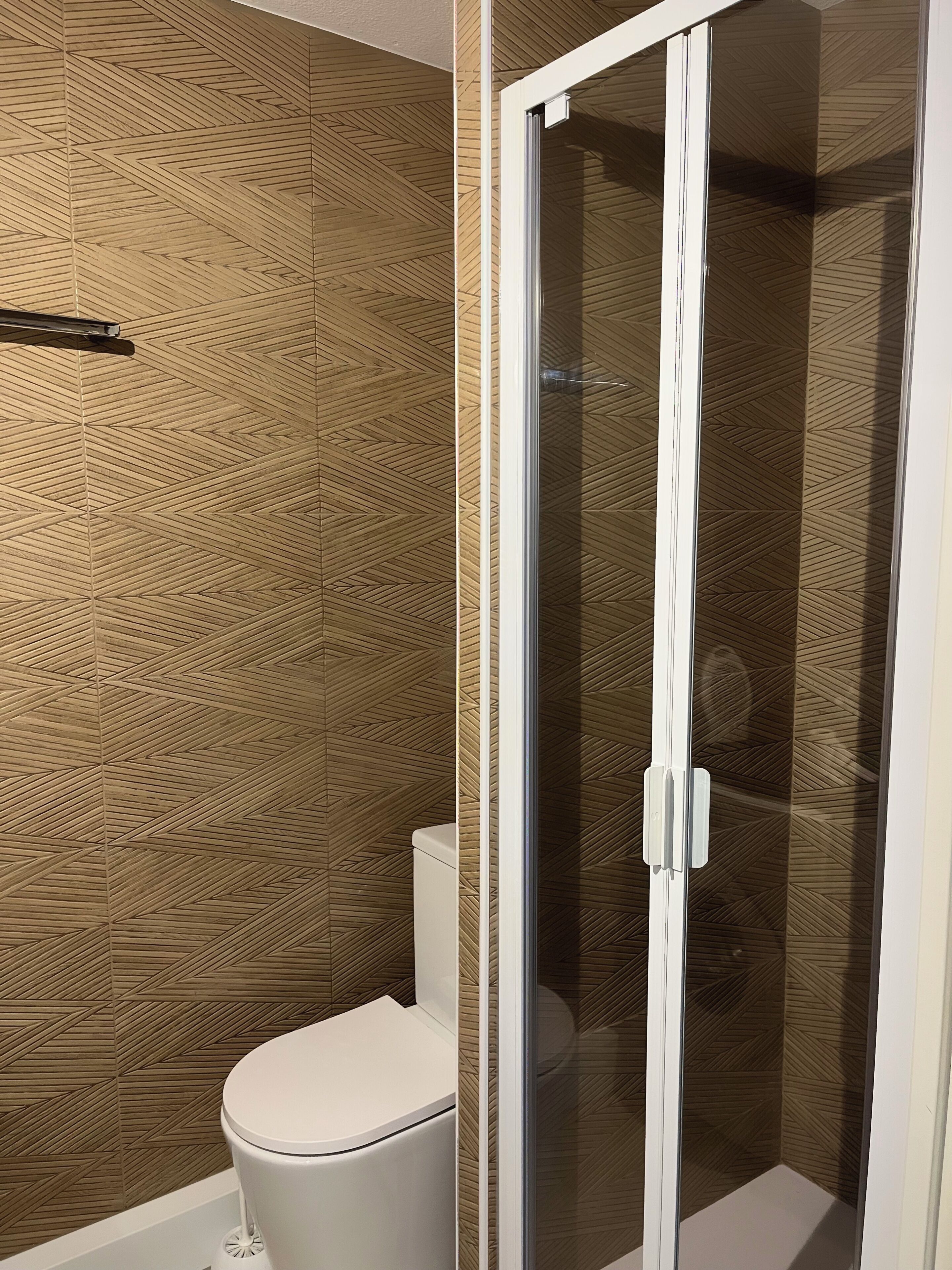 A bathroom with a toilet, a shower enclosure, and a patterned wall.