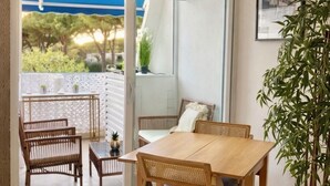 Una habitación con una mesa y sillas de madera, una planta en maceta y un ventanal corredero que da a un área exterior con toldo azul.